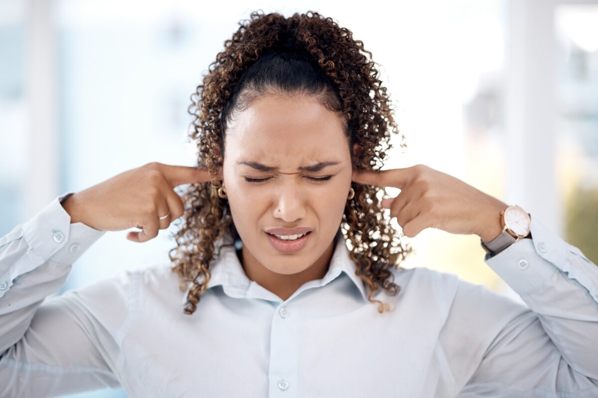 Bruit, fort et femme se bouchant les oreilles aux bruits du bureau alors qu'elle travaille sur un projet. Ann