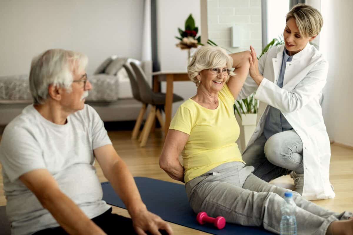Couple mûr faisant de l'exercice à domicile avec l'aide d'un physiothérapeute.