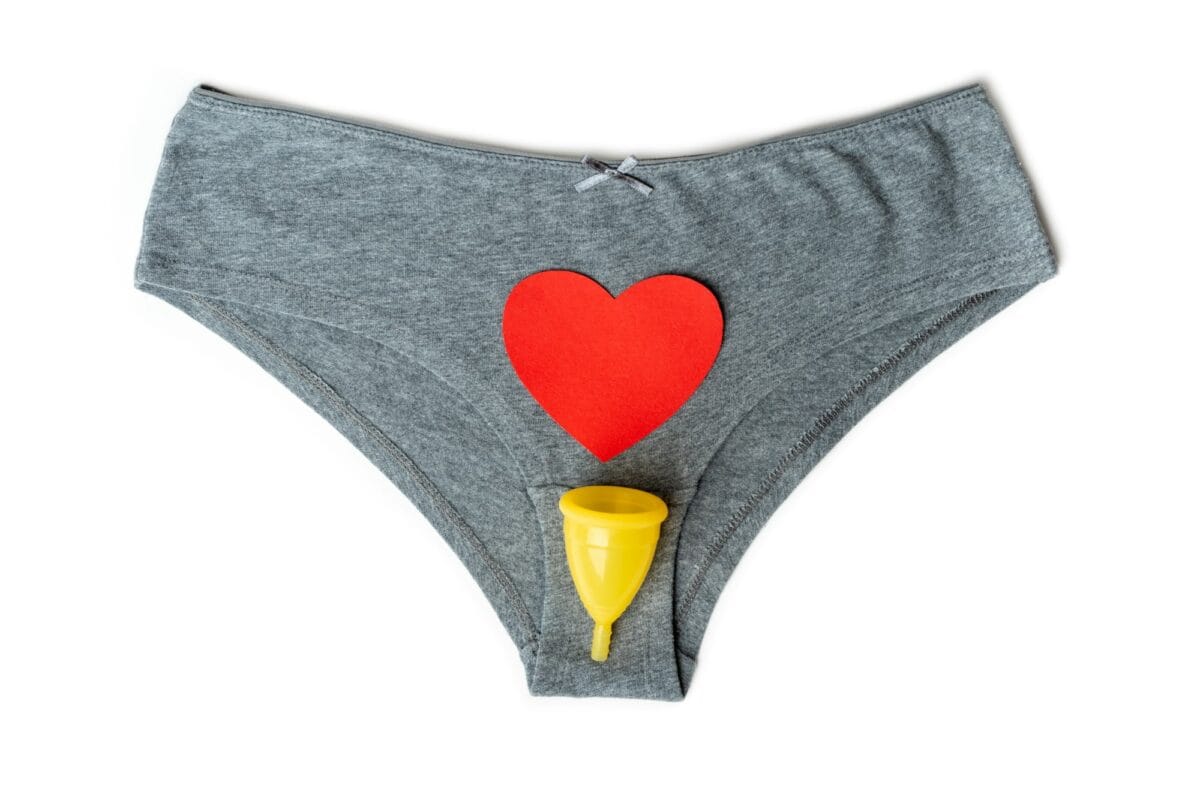 Culotte et sous-vêtements gris pour femme et coupe menstruelle jaune en forme de cœur rouge en guise de gouttes menstruelles.
