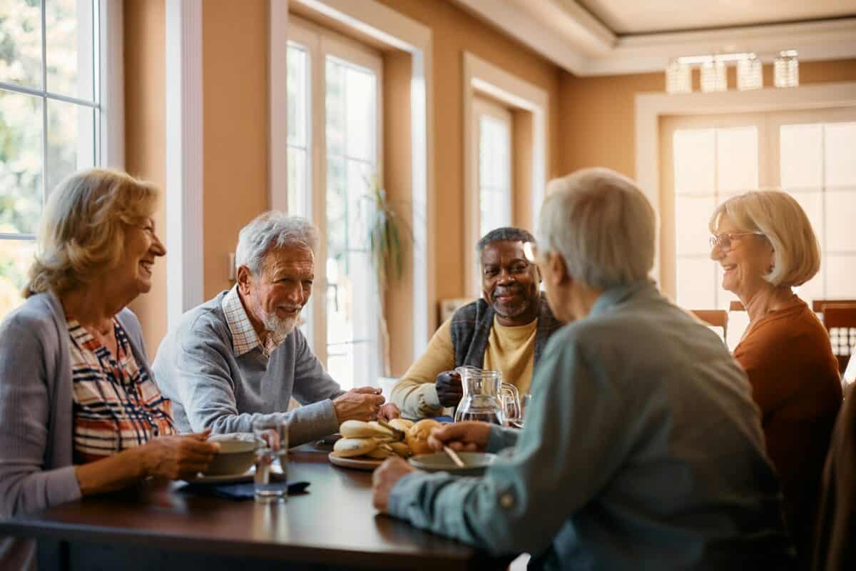 Des personnes âgées heureuses discutent pendant qu'elles déjeunent dans une maison de retraite.