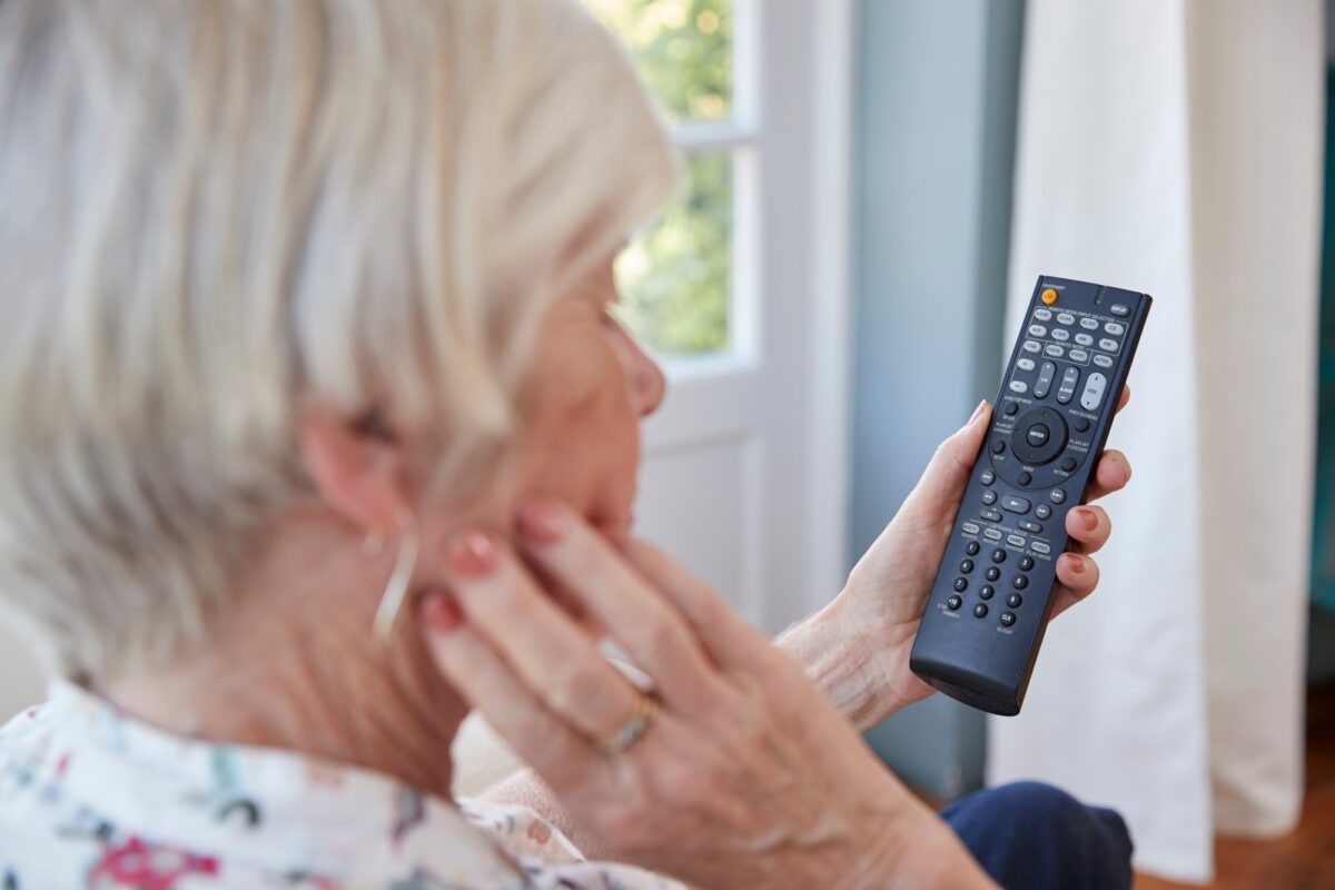 Femme âgée utilisant la télécommande d'un téléviseur, vue par-dessus l'épaule