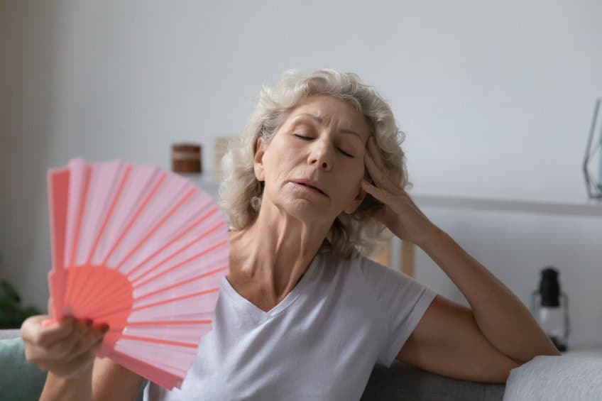 Femme âgée épuisée par la chaleur, la canicule, le temps estival, agitant un éventail à la maison, cherchant à se rafraîchir dans un air trop chaud.