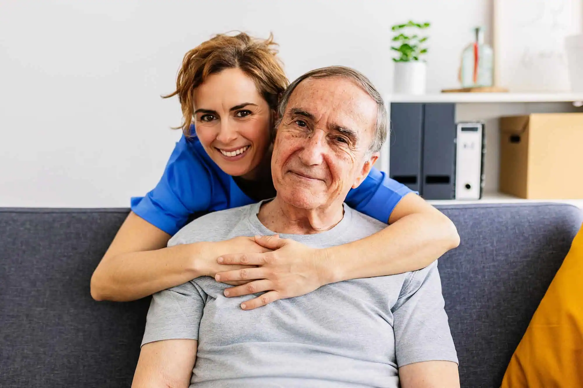 Joyful portrait of mid adult female caregiver hugging senior patient at home