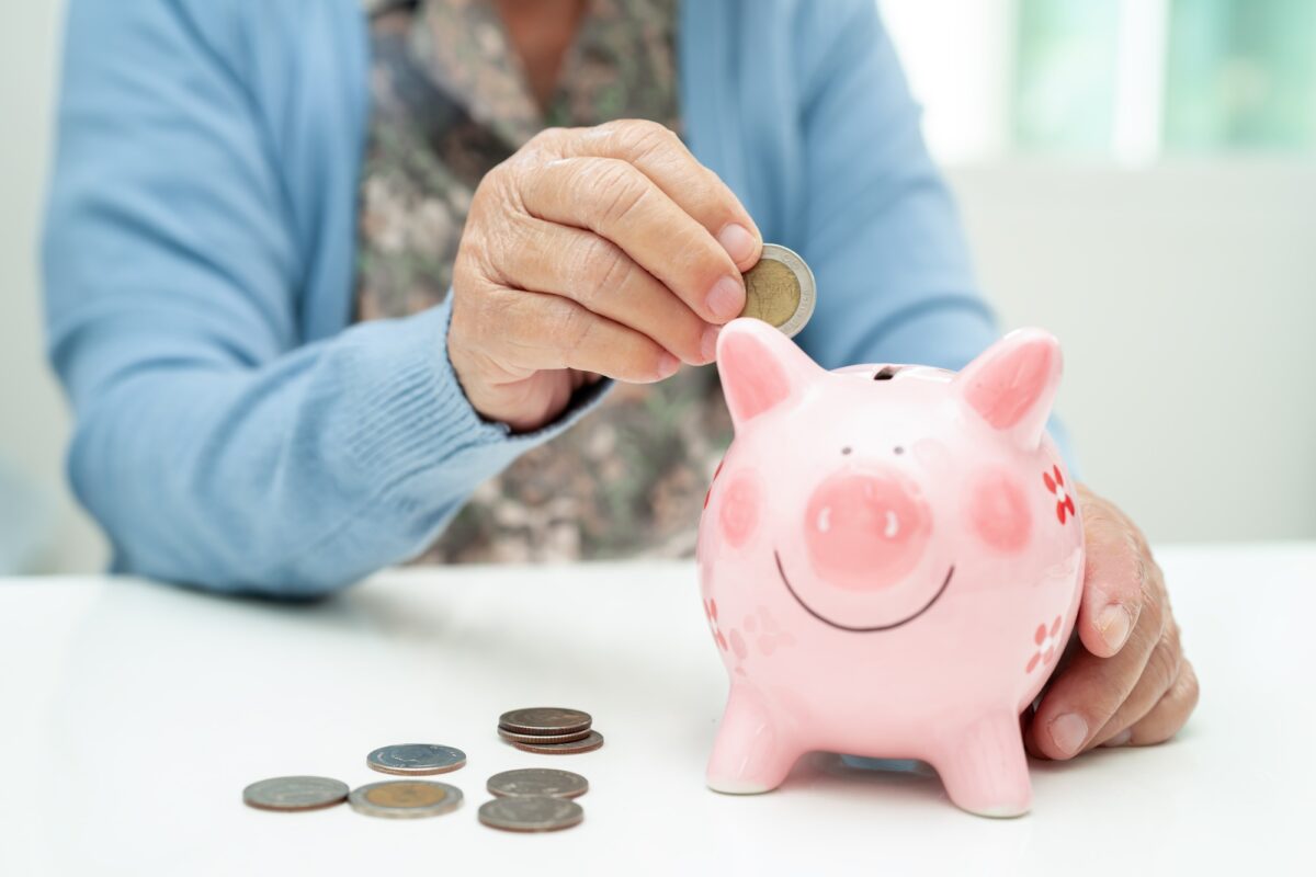 La femme âgée asiatique met une pièce dans une tirelire rose pour économiser de l'argent et de l'assurance, la pauvreté.