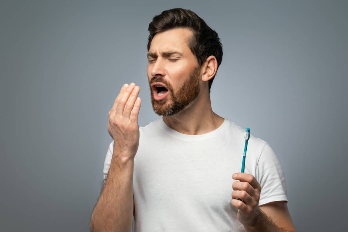 Mauvaise haleine. Un bel homme d'âge moyen vérifie son haleine avec sa main, soufflant dessus, debout au-dessus de lui.