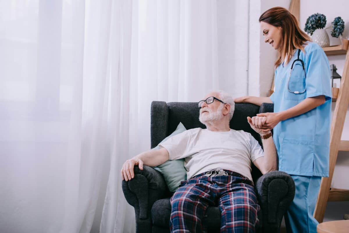 Nurse supporting and holding hand of senior man patient