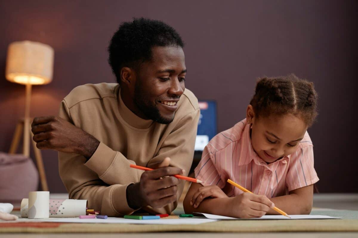 Père et fille faisant des dessins, allongés sur le sol à la maison et souriant joyeusement
