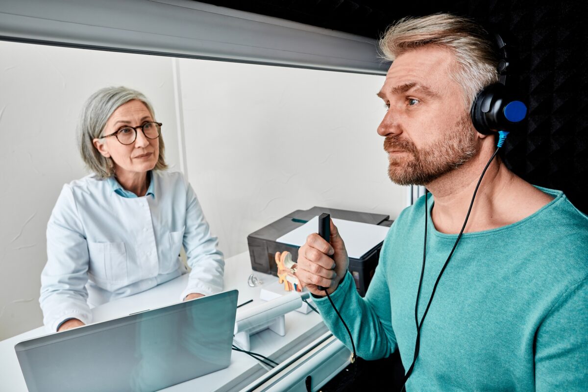 Male patient wearing audiology headphones pressing button of response while audiometric testing in