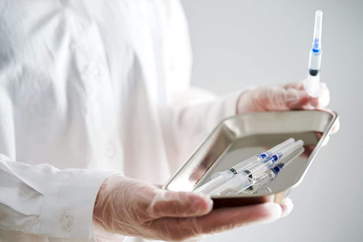 Photo anonymisée des mains d'un médecin tenant un plateau et une seringue avec une aiguille.