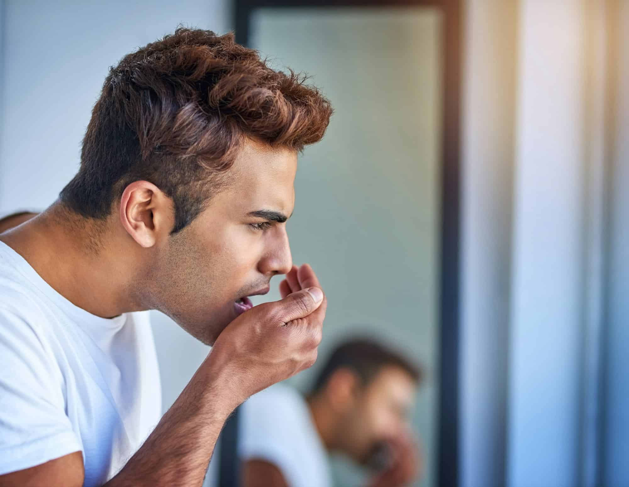 Prise de vue d'un beau jeune homme sentant son haleine lors de sa toilette matinale.