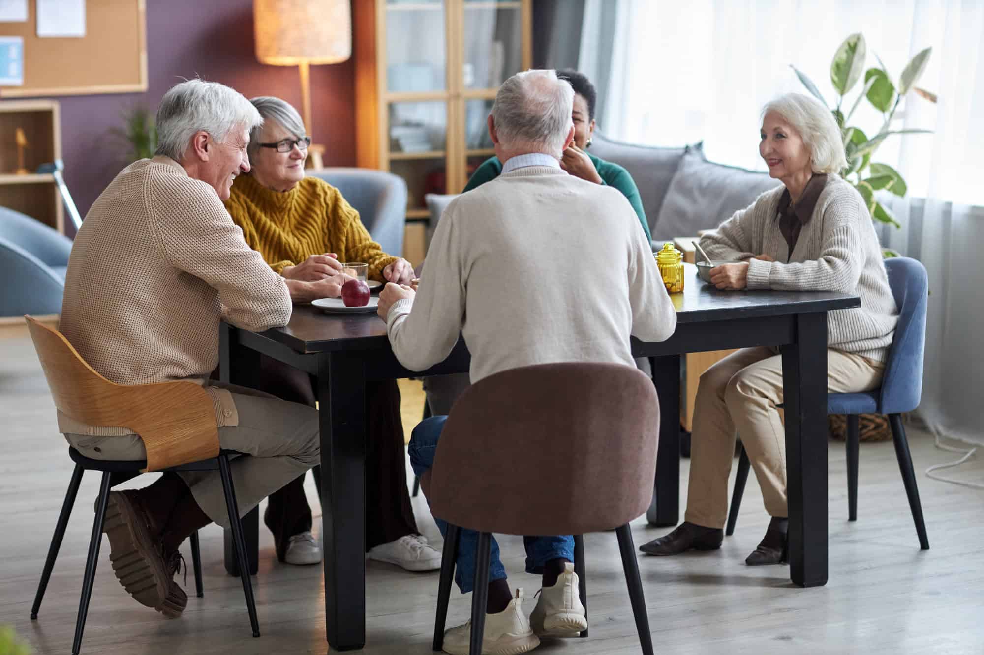 Seniors sitting at table together and smiling happily in retirement home