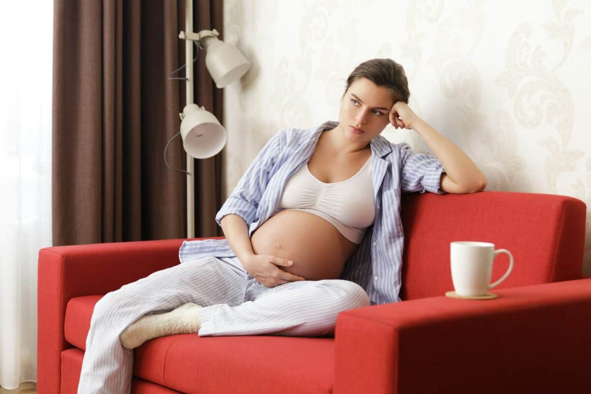 Tired pregnant woman sitting with on the red sofa