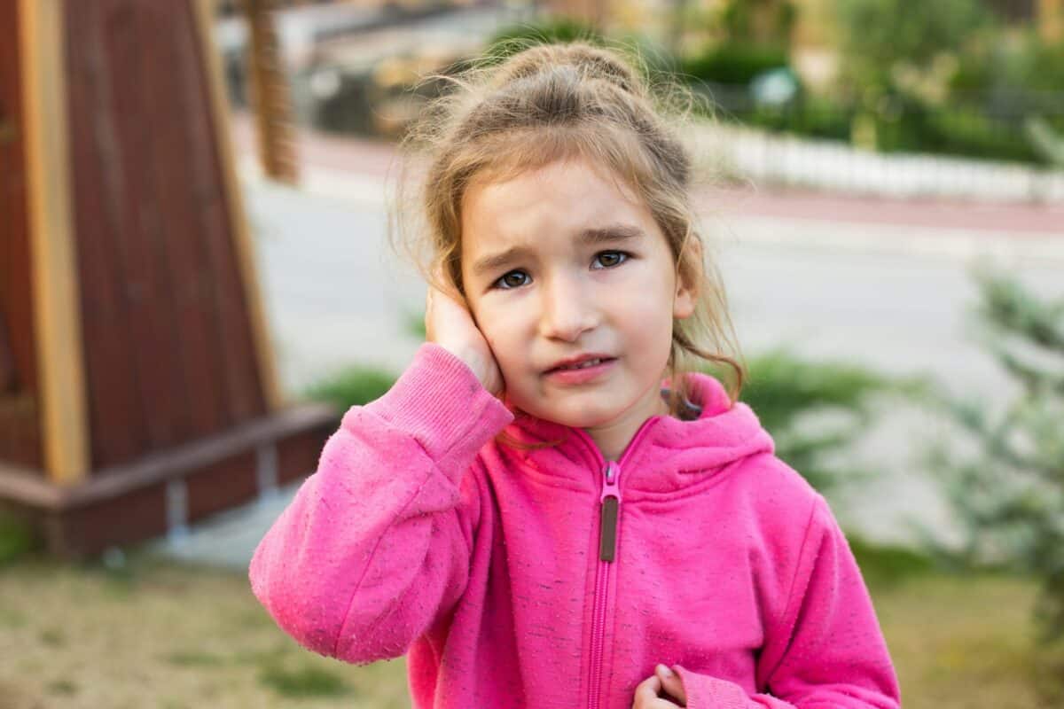 Une petite fille vêtue d'un sweat à capuche rose, le visage triste et en larmes, se tient l'oreille. Douleur à l'oreille