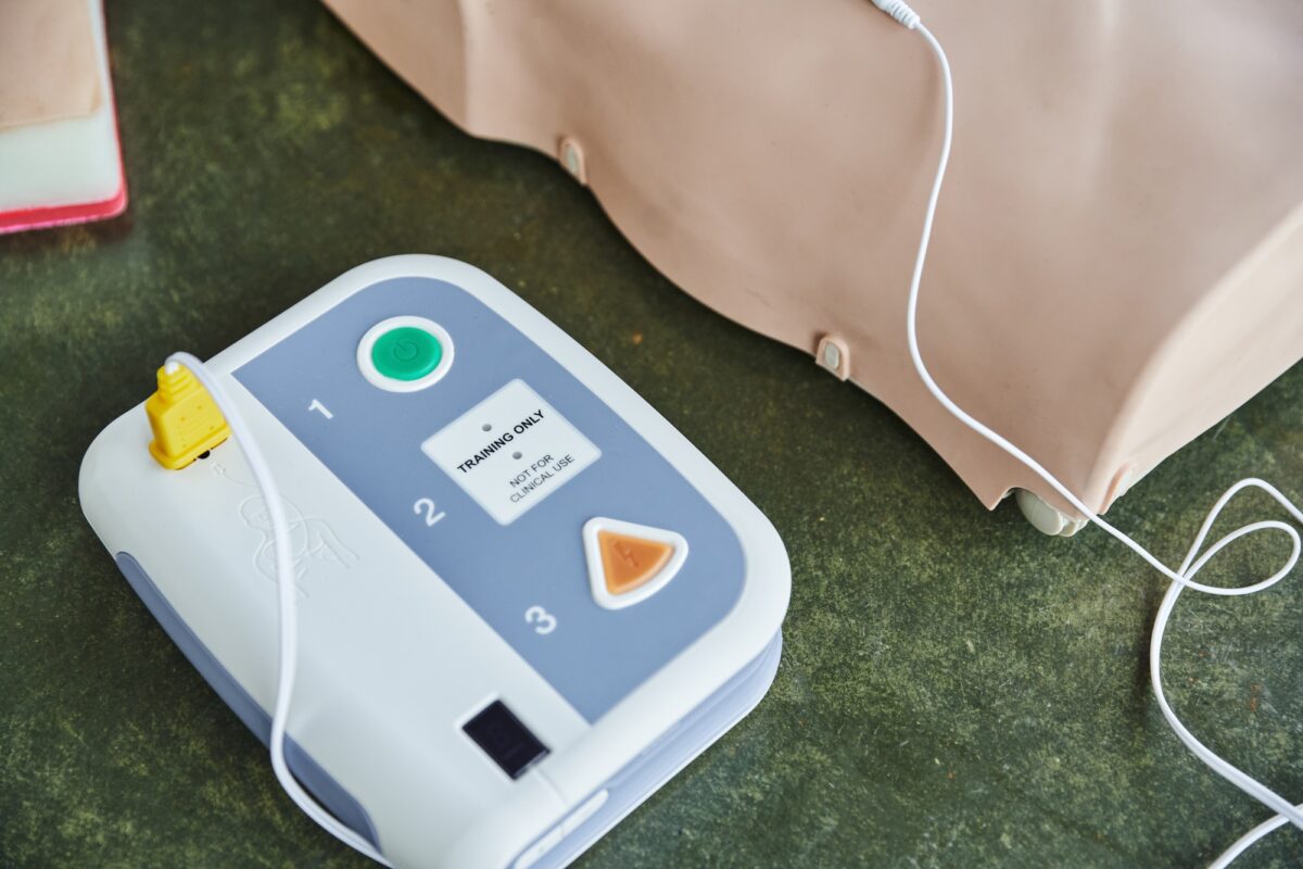 Vue en plongée d'un défibrillateur externe automatisé moderne près d'un mannequin de RCP en formation.