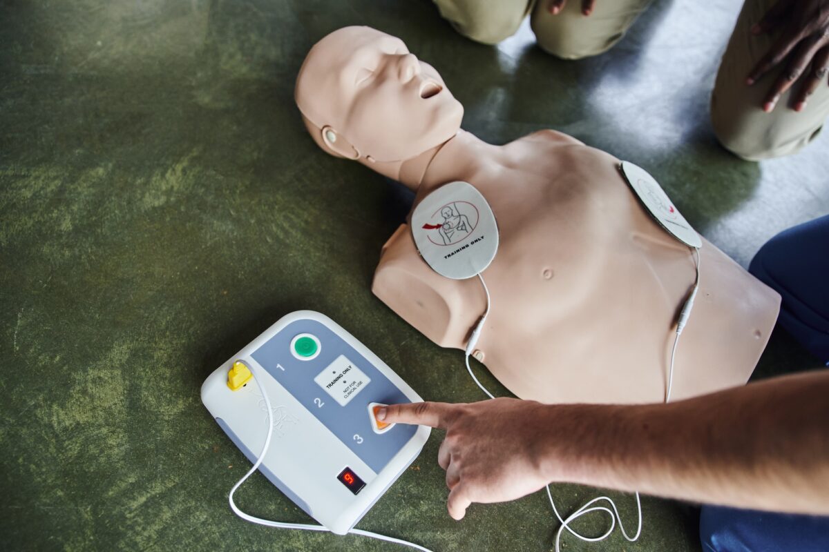 Vue partielle d'un instructeur médical professionnel utilisant un défibrillateur sur un mannequin de RCP près d'un jeune.